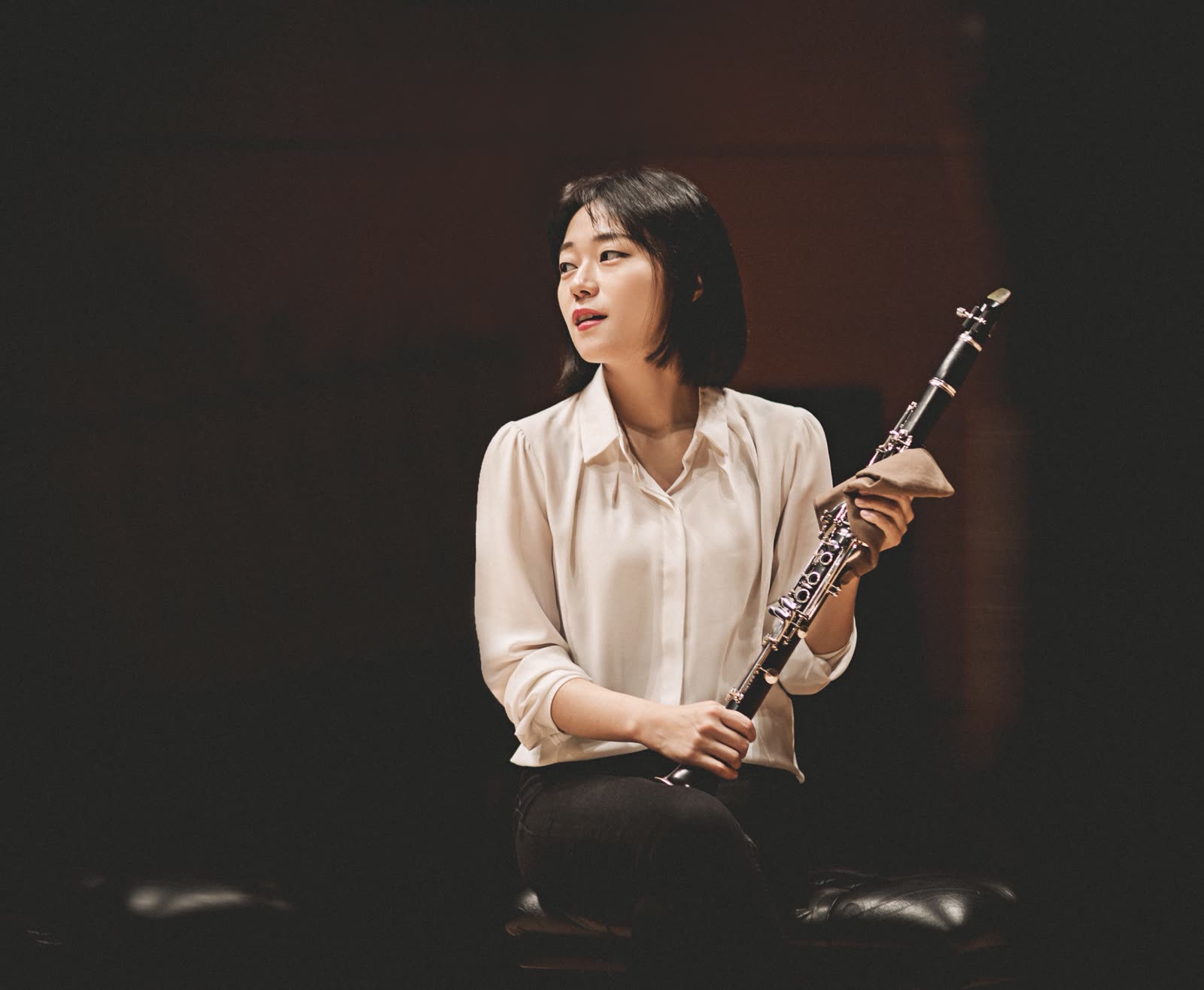 MinYoung Lee seated on stage, holding a clarinet and looking to the side.