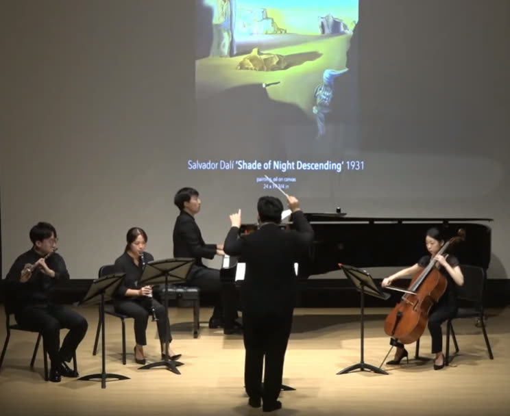 A conductor leads flute, clarinet, piano and cello beneath a projection of Salvador Dalí’s Shade of Night Descending.